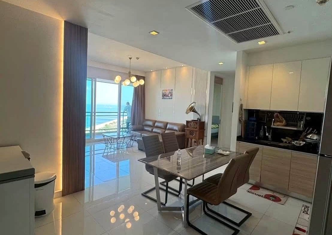 Bright open-plan living space with dining area, kitchen, and ocean-view balcony seen through glass doors at the far end.