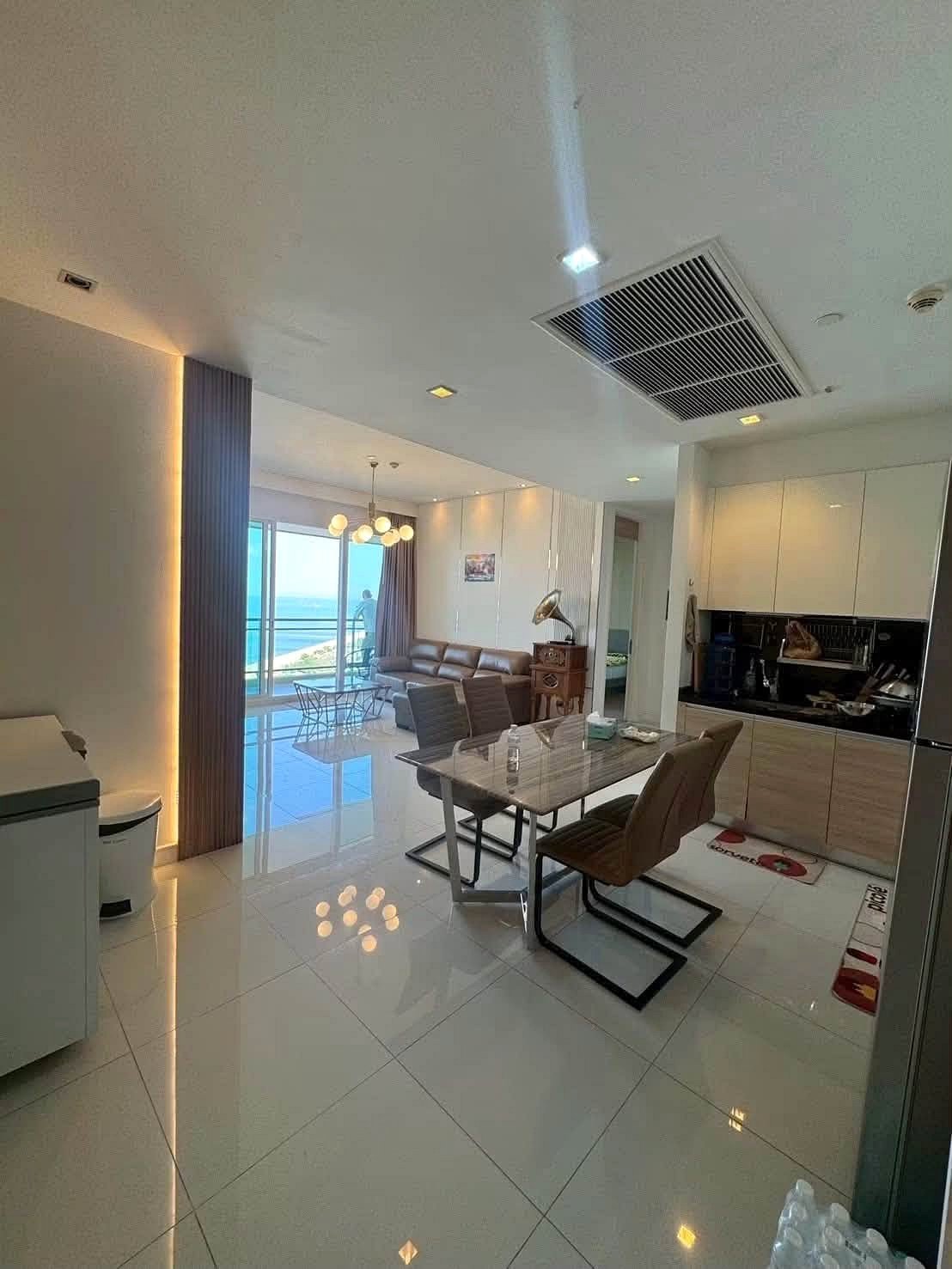 Reflectiom_Jomtien_2Bed_Dlc625_14 Bright open-plan living space with dining area, kitchen, and ocean-view balcony seen through glass doors at the far end.