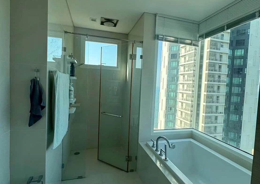 Bright, modern bathroom with a glass-enclosed shower and a white tub by a large window overlooking city high-rises.