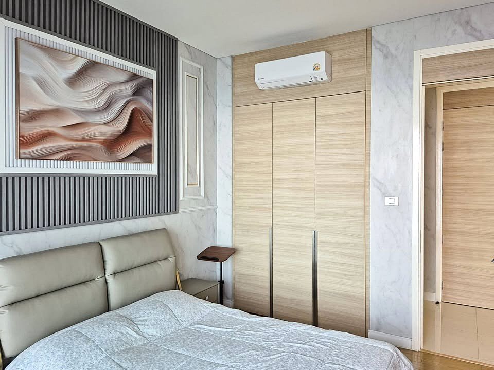 Modern bedroom with a gray upholstered bed, wooden built-in wardrobe, wall-mounted AC, and abstract framed art above the headboard.