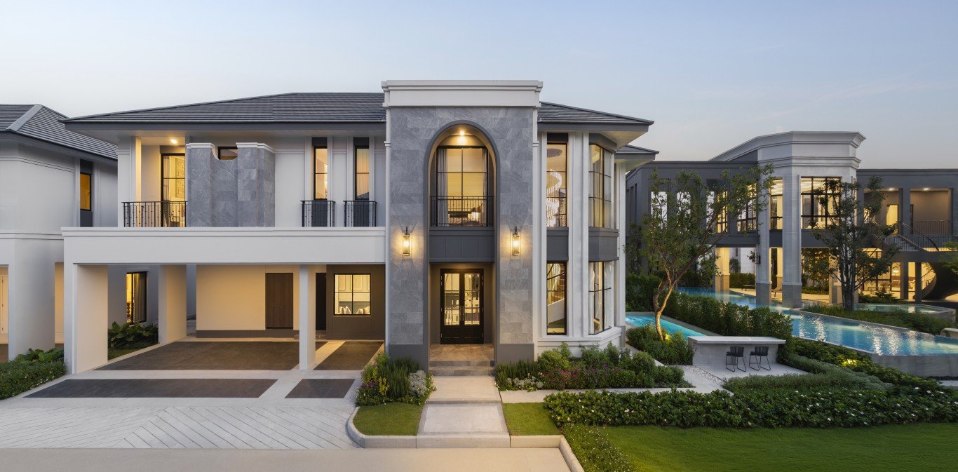 Rekha Pattaya-Motorway 11 Front view of a modern luxury townhouse with a gray stone façade, arched central window, and landscaped entry, with a pool area in the background.