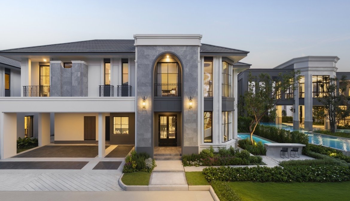 Front view of a luxury residential complex featuring a central arched window, balconies, and a manicured entrance lawnled driveway.