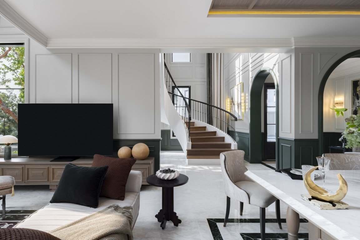 Elegant living area with a flat-screen TV on a wooden console, sofa cushions, and a marble floor bathed in natural light from a large window.