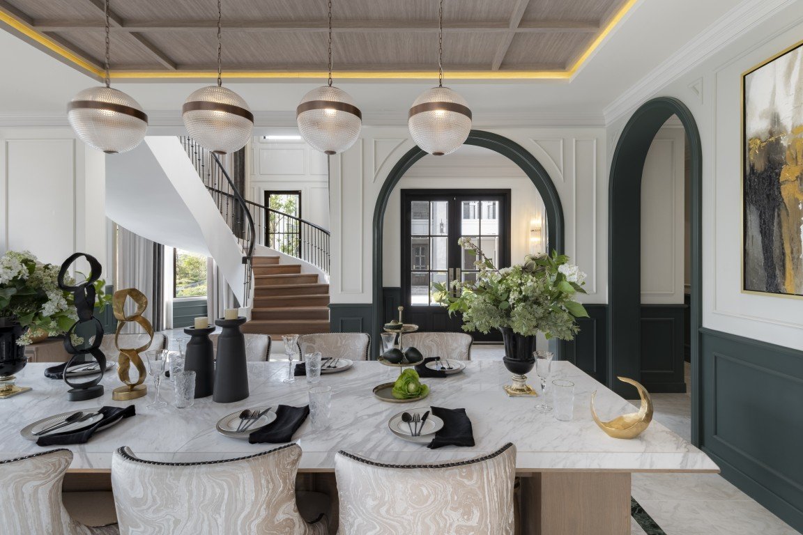 Elegant dining room with a marble table set for a meal, decorative sculptures, and a curved staircase in the background