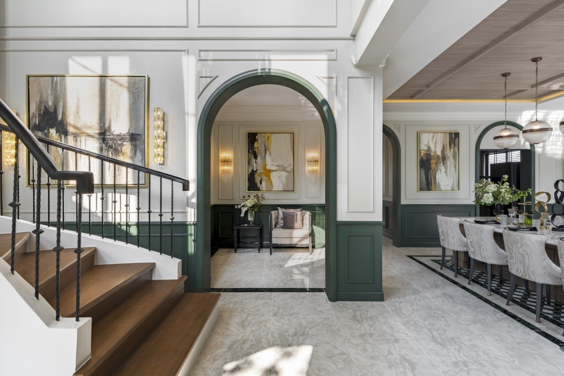 Elegant two-tone foyer with a wooden staircase on the left, a green arched doorway to a seating nook, and a formal dining area to the right.