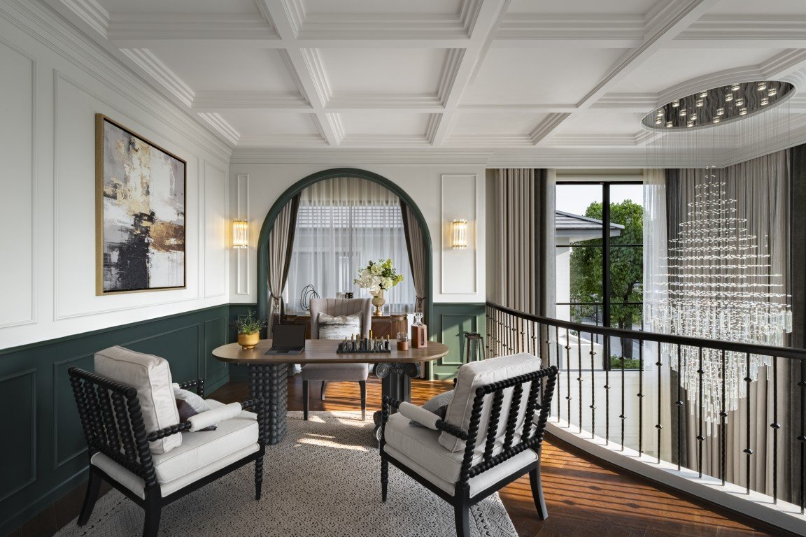 Elegant balcony lounge with two cushioned chairs around a round wooden table, an arched window, and a sparkling crystal chandelier.