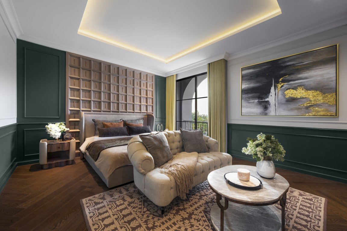 Luxurious bedroom with a tufted beige bed, green paneled walls, gold-accented ceiling lighting, and a cream sofa facing a marble coffee table.