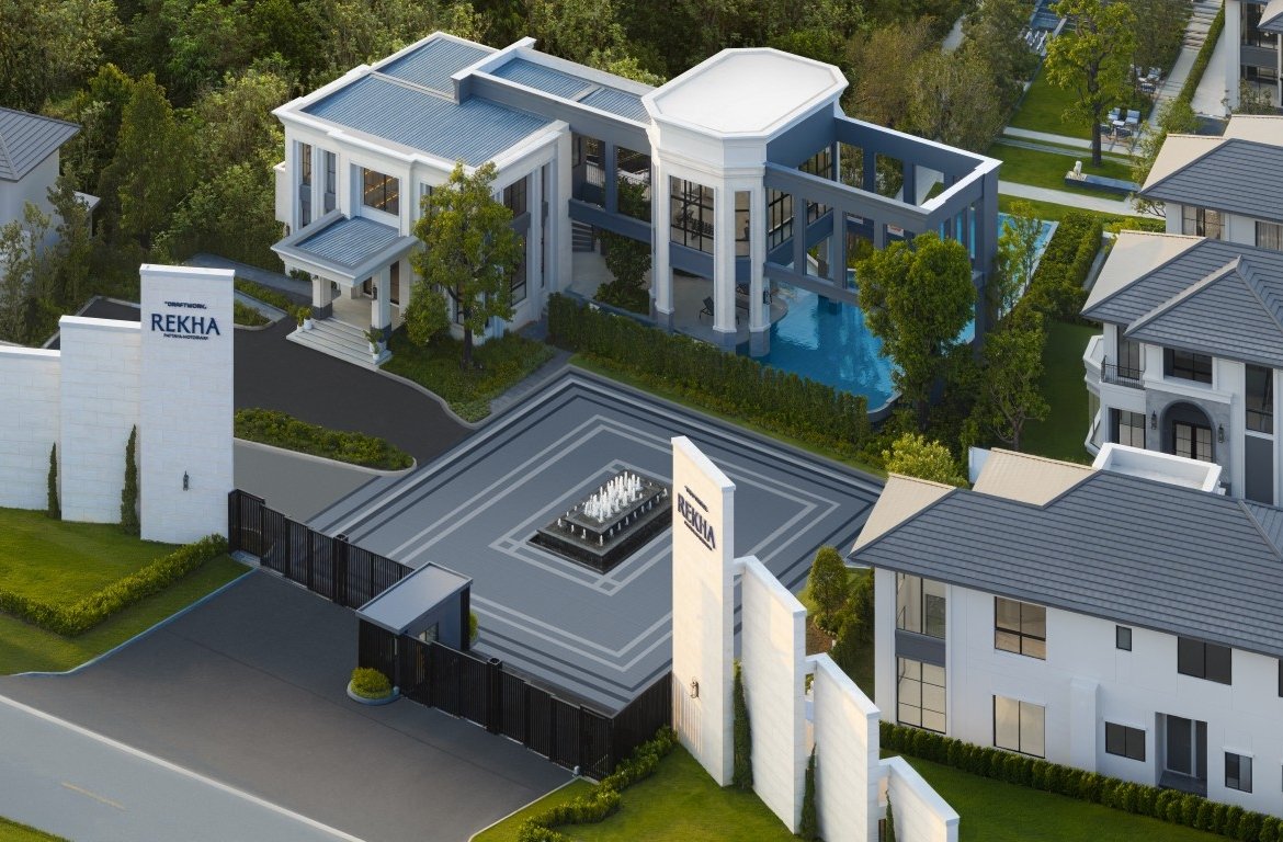 A modern gated estate with white buildings, a central tiled plaza featuring a fountain, and a gate labeled REKHA.