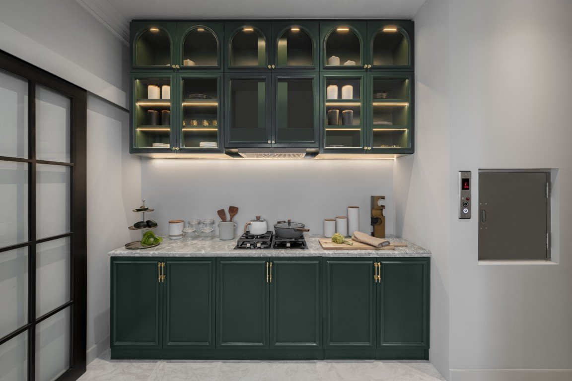 Modern kitchen with dark green cabinets, marble countertop, and a stovetop with pots.
