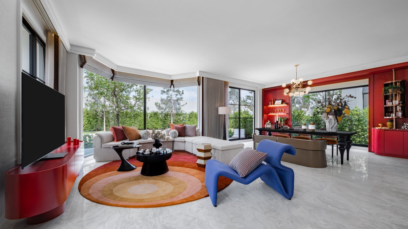 Rekha Pattaya-Motorway 33 Spacious living room with red accents, a circular orange rug, and a large beige sectional by floor‑to‑ceiling windows overlooking greenery.