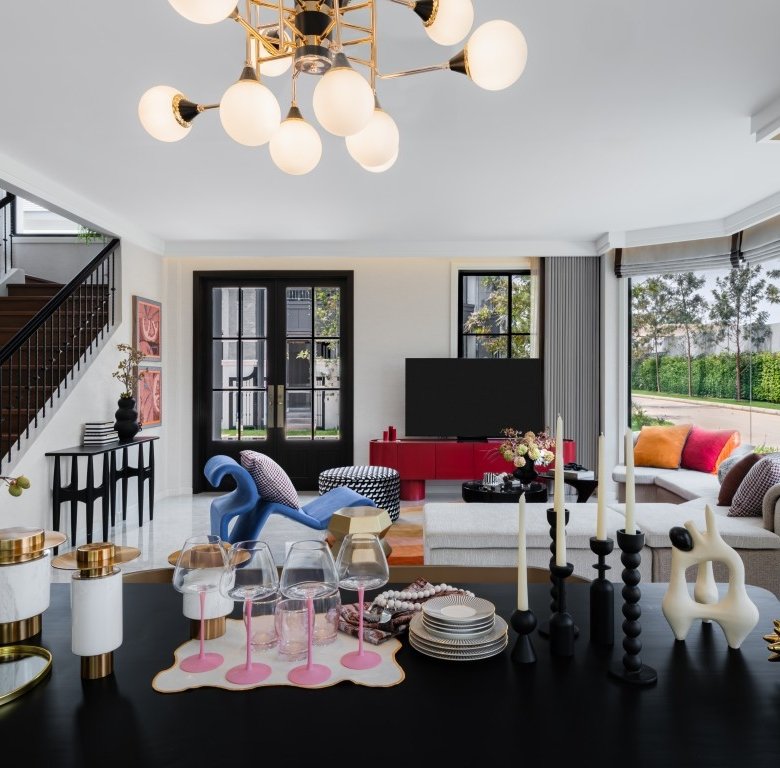 Open living and dining area with a modern chandelier staircase on the left and a table set with glasses and candles in the foreground