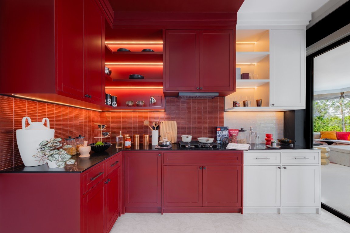 Modern kitchen with deep red lower and upper cabinets, maroon tile backsplash, and warm LED lighting along open shelves and counter.