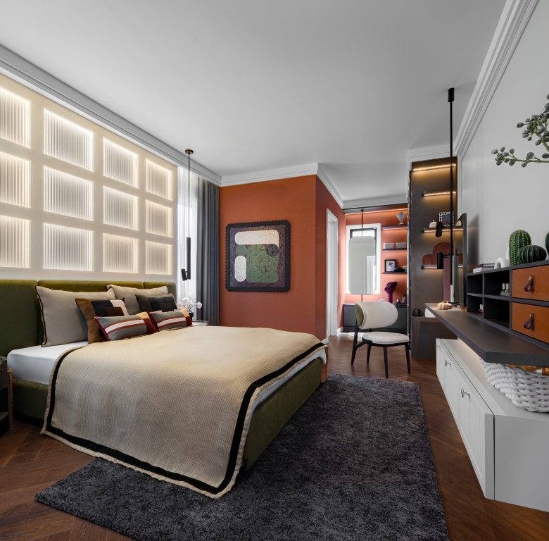 Contemporary hotel style bedroom with a green upholstered bed beige bedding and an orange accent wall on the far side