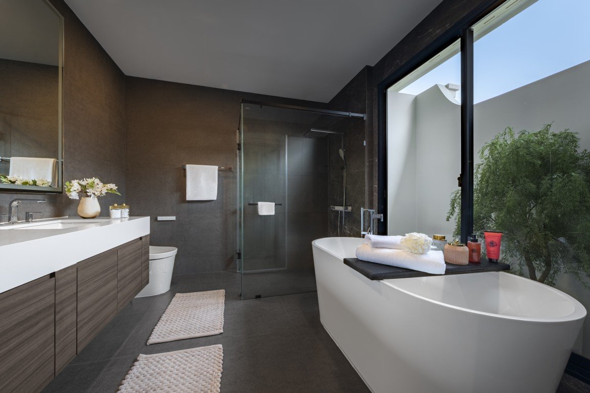 Modern bathroom with a white freestanding tub by a large window, a glass-enclosed shower, and a double vanity.