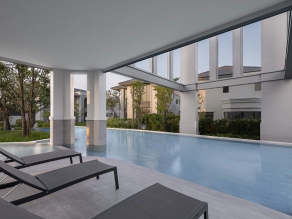 Modern covered poolside area with three black lounge chairs along a light tile deck, reflecting a calm blue pool and surrounding greenery.