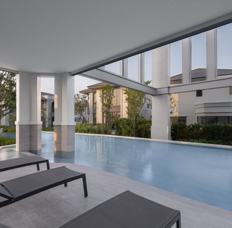 Modern covered poolside area with three black lounge chairs along a light tile deck reflecting a calm blue pool and surrounding greenery