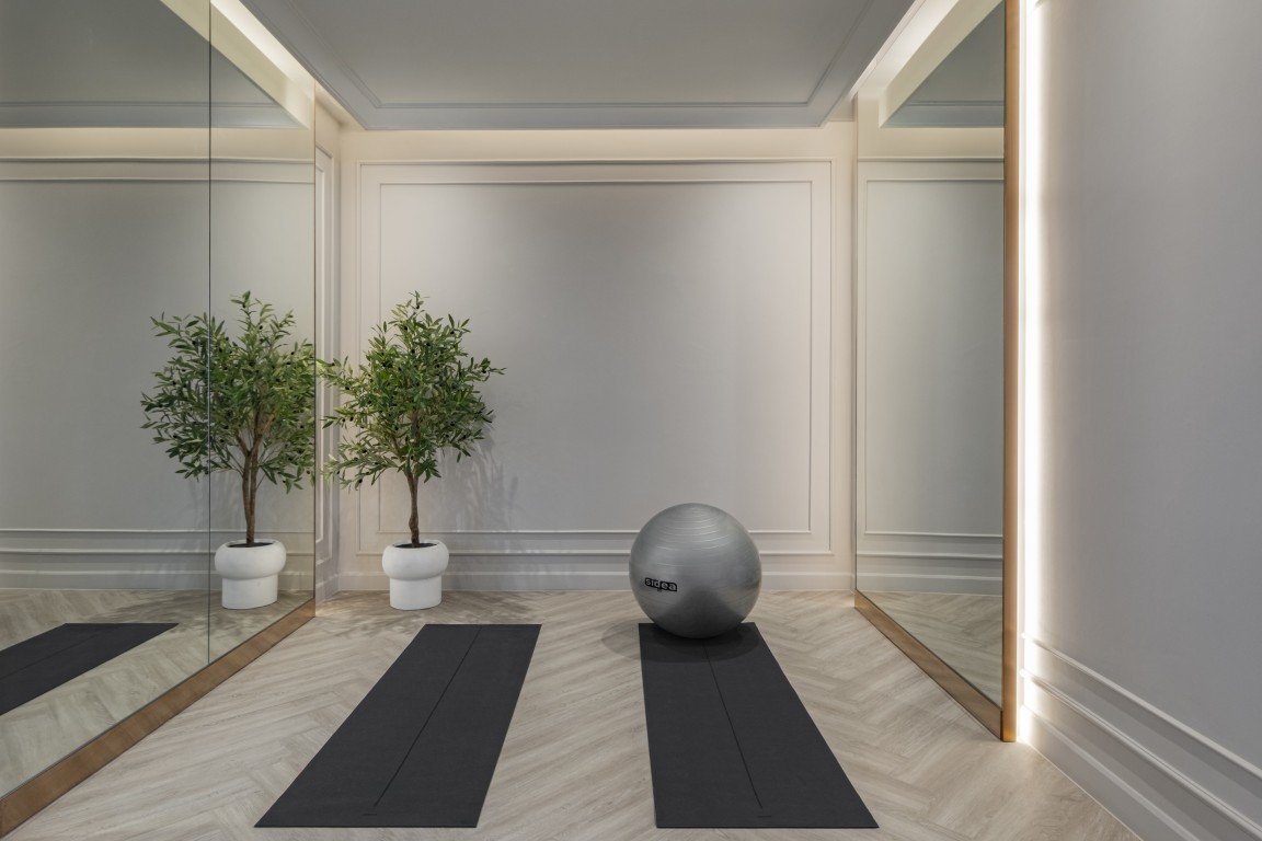 Minimalist yoga area with two black mats, a gray exercise ball, and two potted trees reflected in mirrors.
