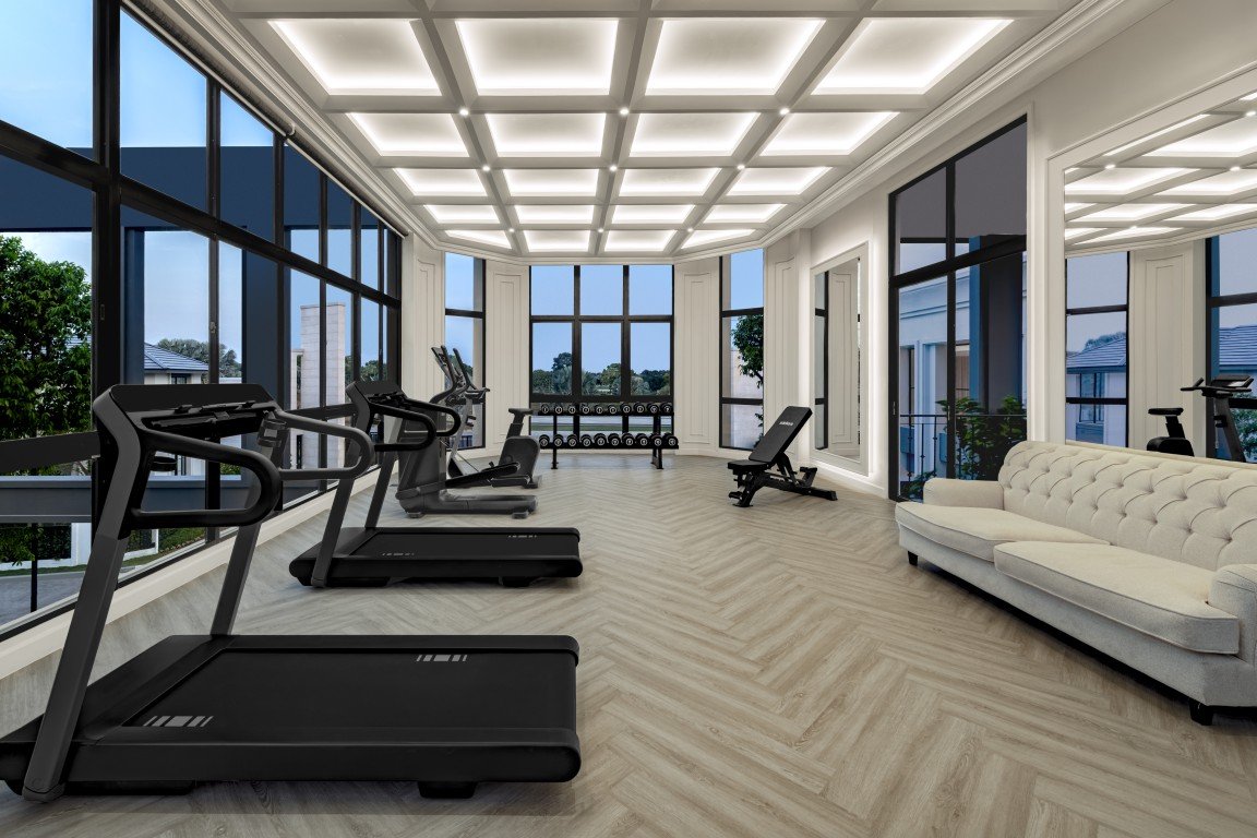 Bright gym interior with treadmills along large windows and a light wood floor, plus a beige sofa on the right.