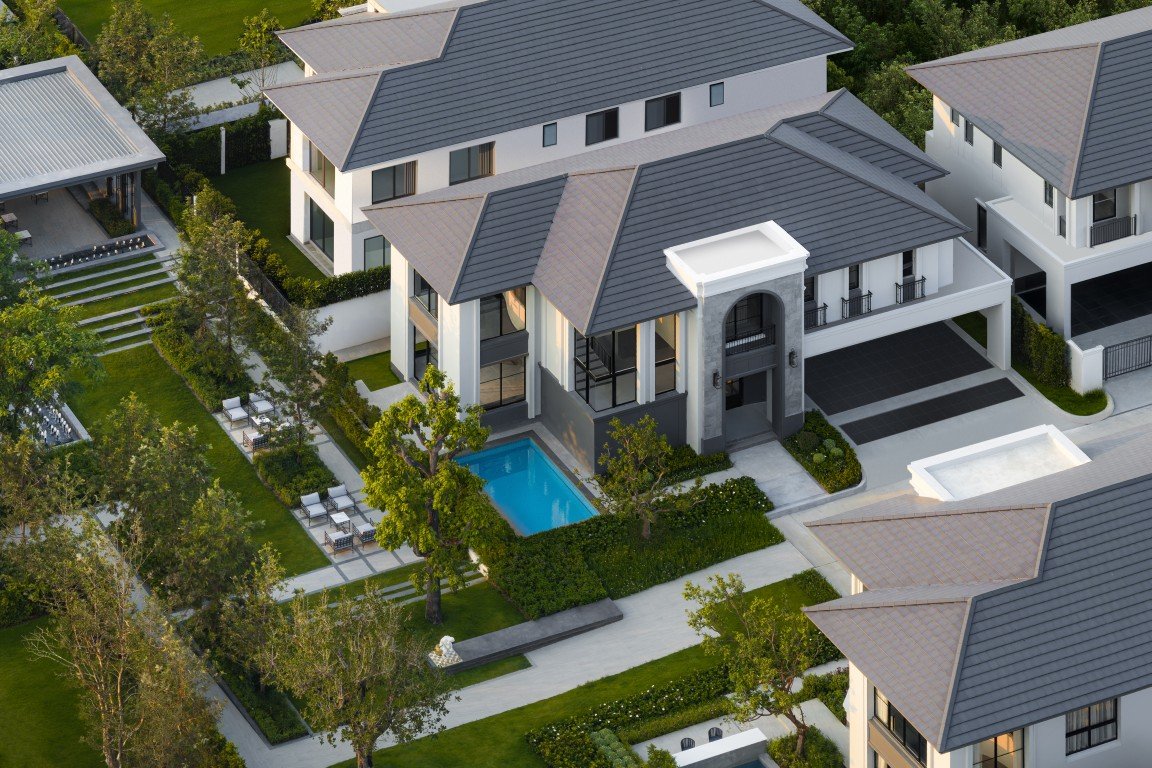 Aerial view of a modern residential complex with white buildings, gray sloped roofs, a central rectangular pool, and neatly landscaped gardens.