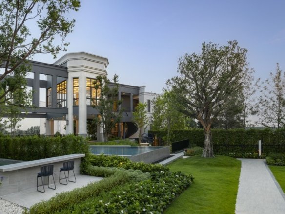 Modern two-story home with large windows and a rectangular pool, set in a manicured garden.