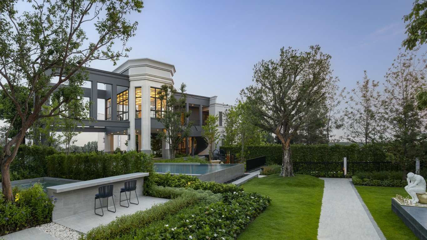 Rekha Pattaya-Motorway 9 Modern two-story residence with large windows, a rectangular pool, and manicured landscaping.