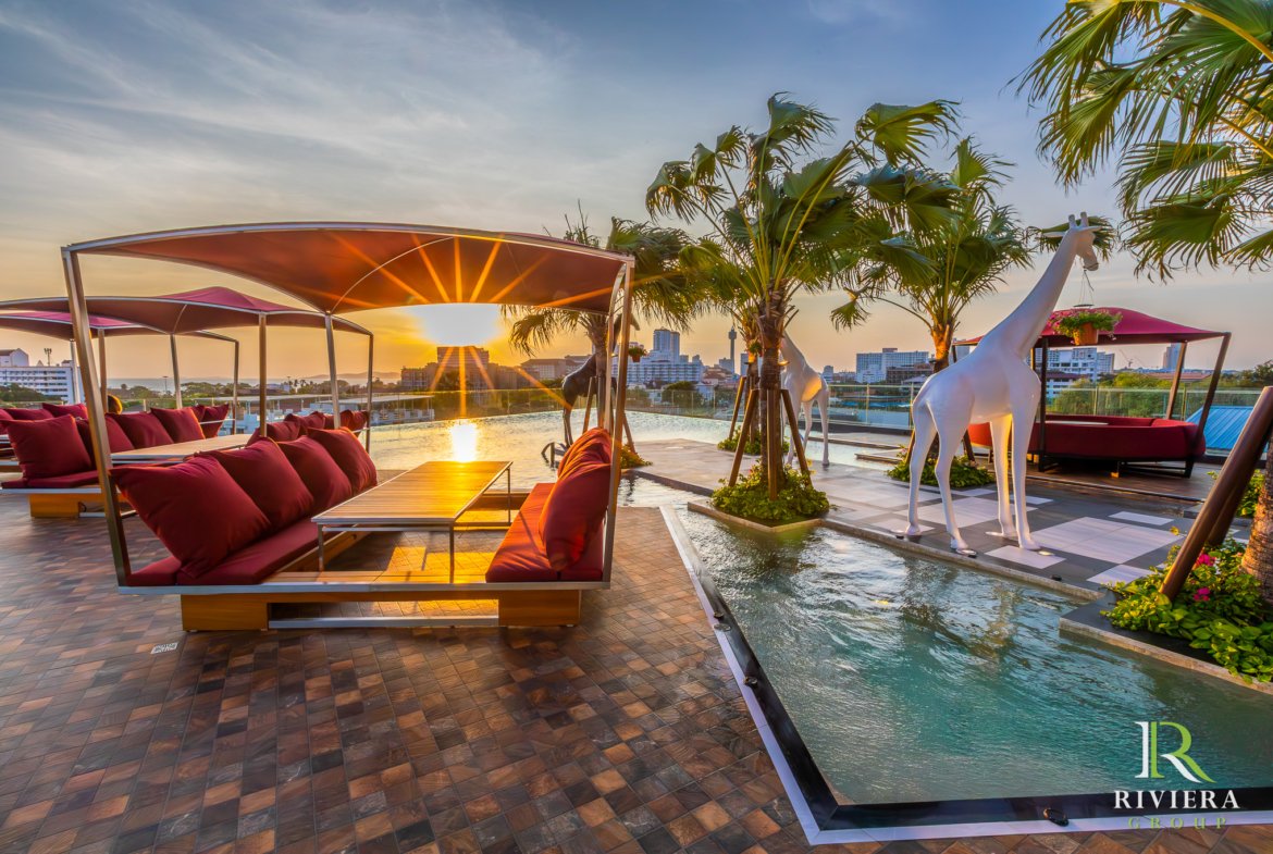 Luxurious rooftop lounge at sunset with red-cushioned seating, palm trees, and white horse sculptures beside a pool.