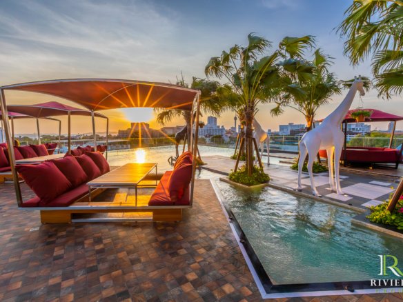 Sunset rooftop lounge with red-cushioned seating under canopies, palm trees, and white horse sculptures by a water feature.