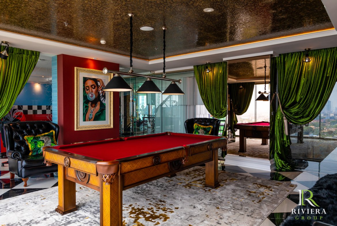 Luxurious game room with red felt pool table, black tufted chairs, and green velvet curtains with a city view outside