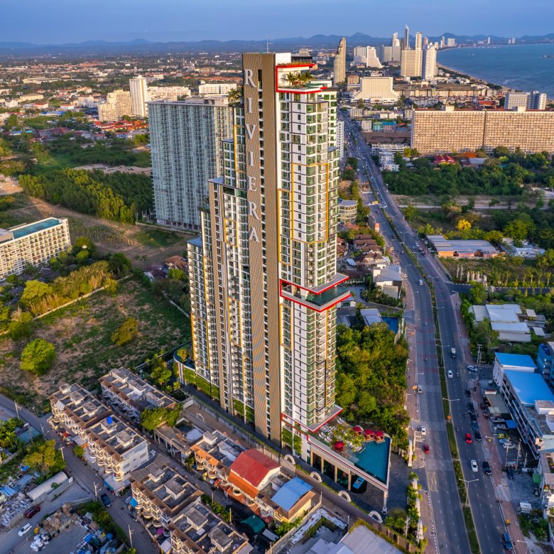 Aerial view of a coastal city with a tall modern residential tower labeled Riviera surrounded by buildings streets and the ocean in the distance