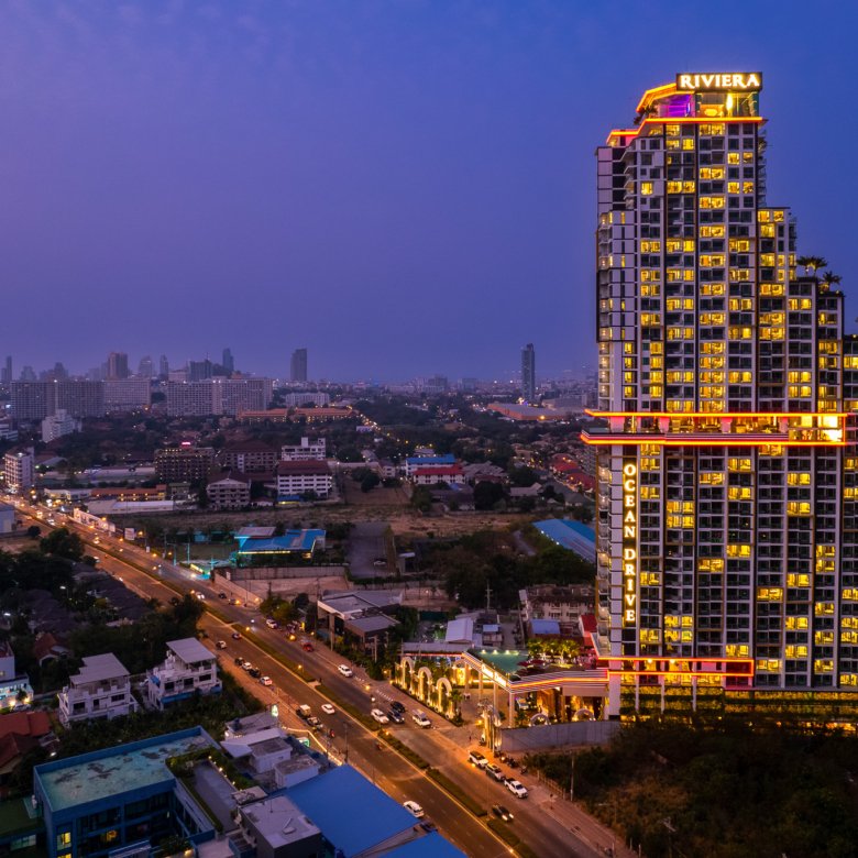 Night aerial view of a tall neon lit hotel with a RIVIERA sign on top overlooking a city at dusk