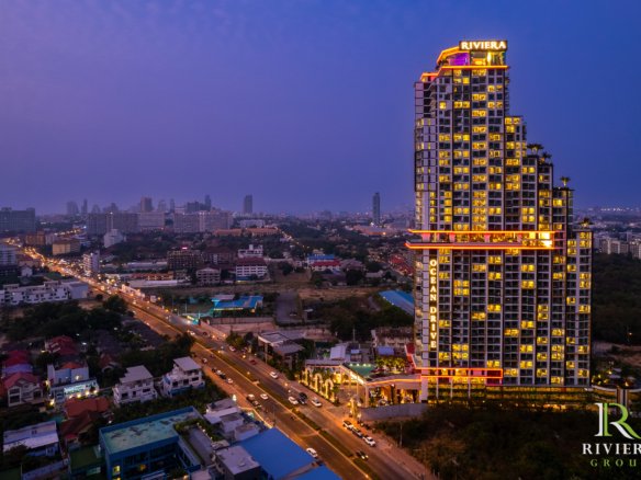 Dusk cityscape with a tall, neon-lit Riviera hotel tower dominating the skyline and colorful hotel lights in surrounding buildings.