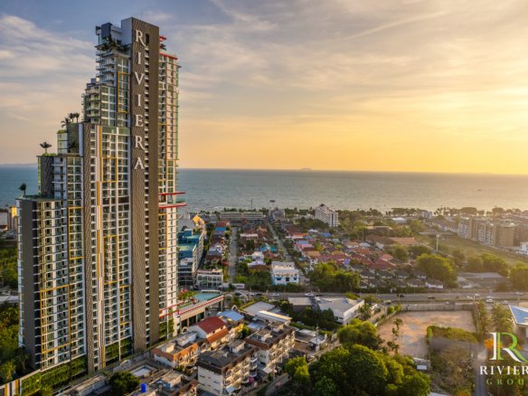 Tall modern beachfront condo tower with the Riviera logo in the lower-right, overlooking a coastal town at sunset.（informative）