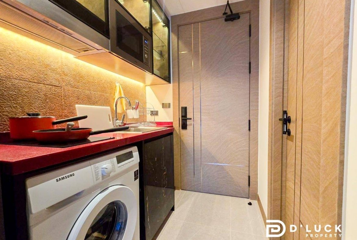 Compact modern kitchenette with a red countertop, front-loading Samsung washing machine, black lower cabinets, and a wall-mounted microwave above the counter.