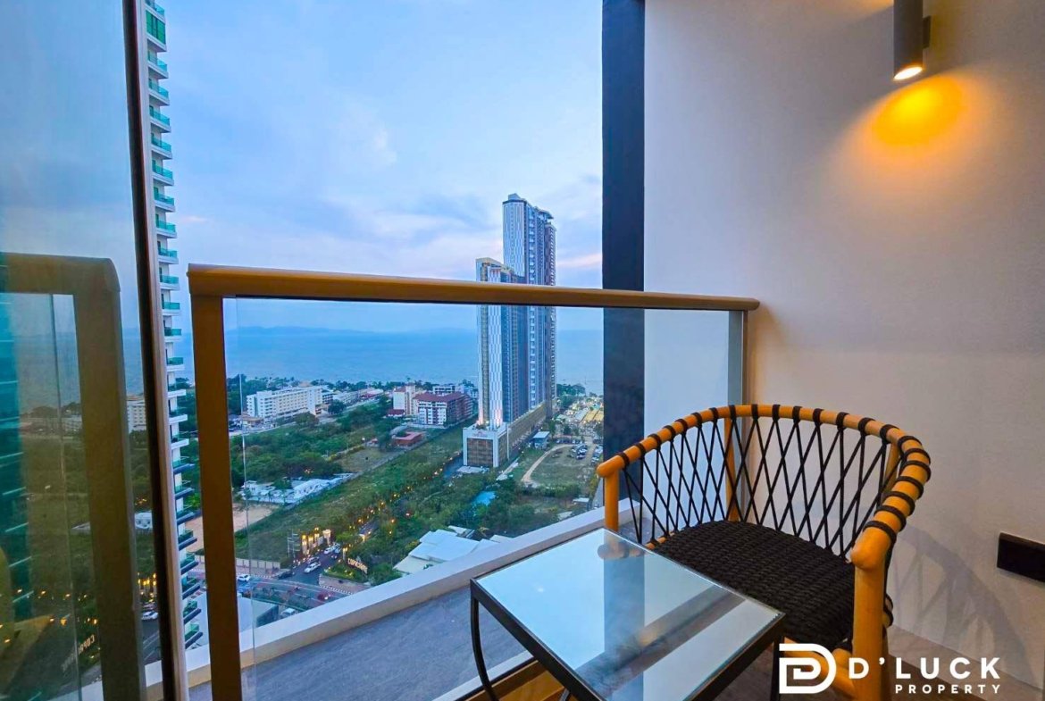 Balcony seating area with a glass table and woven chair, overlooking a city and the sea horizon.