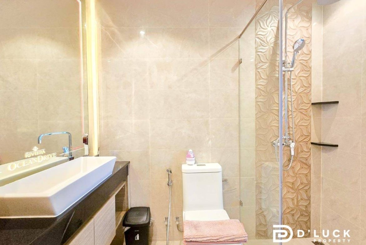 Contemporary bathroom with a rectangular white sink on a dark countertop, large mirror, and a toilet with a pink towel folded on top.