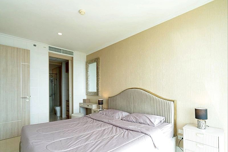 Hotel bedroom with a large bed, beige headboard, two nightstands with lamps, and an open doorway to the en-suite bathroom on the left.