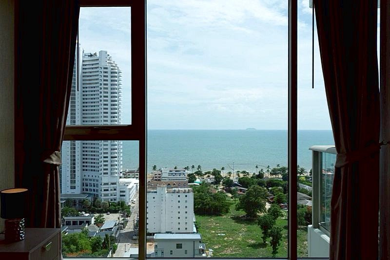 View from a hotel room window overlooking the sea, with high-rise buildings to the left and a green park below.