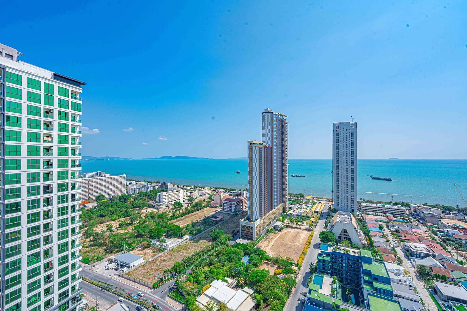 Riviera_Ocean_Drive_Studio_Rent_Rdl360_11 Aerial view of a coastal city with high-rise buildings along the shoreline and a blue ocean in the background, under a clear sky.