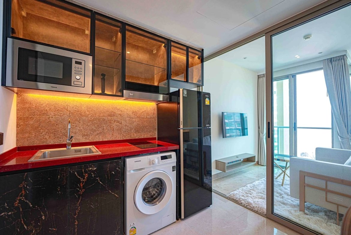 Modern kitchen with black marble lower cabinets, red countertop, stainless microwave, and front-loading washing machine.