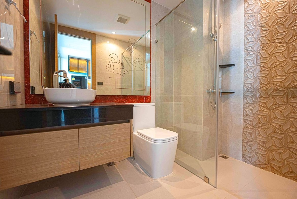 Modern bathroom with a wooden vanity, white vessel sink, large mirror, glass shower, and decorative beige tiled walls.