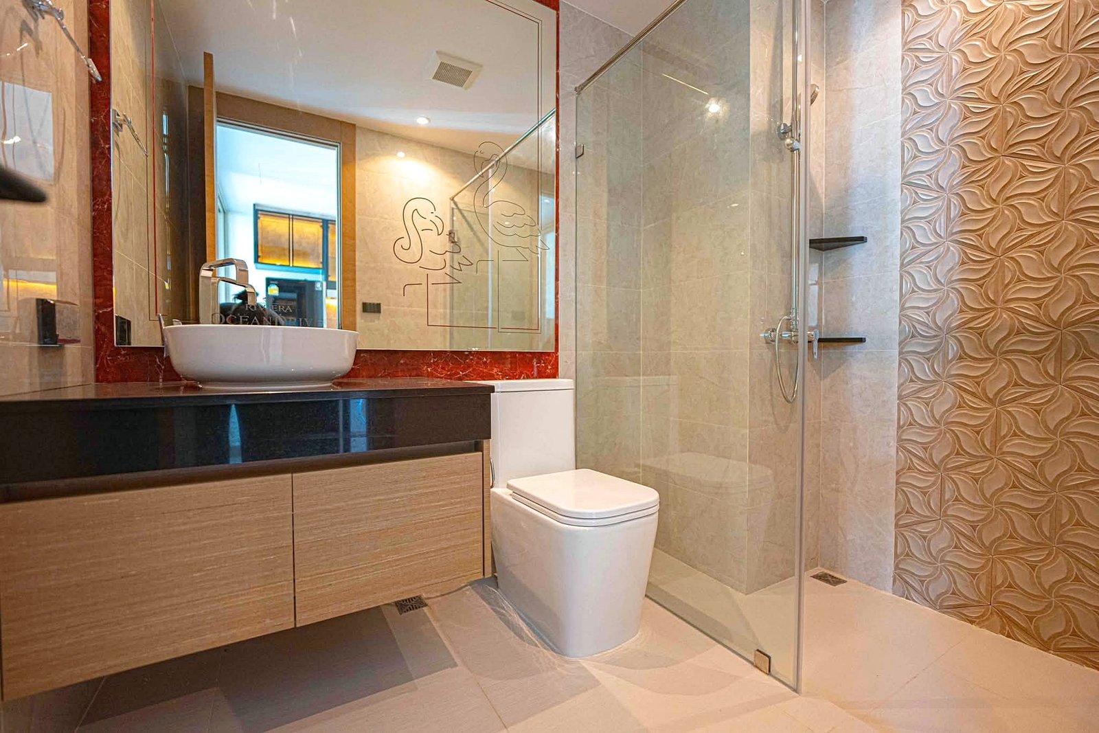 Riviera_Ocean_Drive_Studio_Rent_Rdl360_4 Modern bathroom with a wooden vanity, white vessel sink, large mirror, glass shower, and decorative beige tiled walls.",
