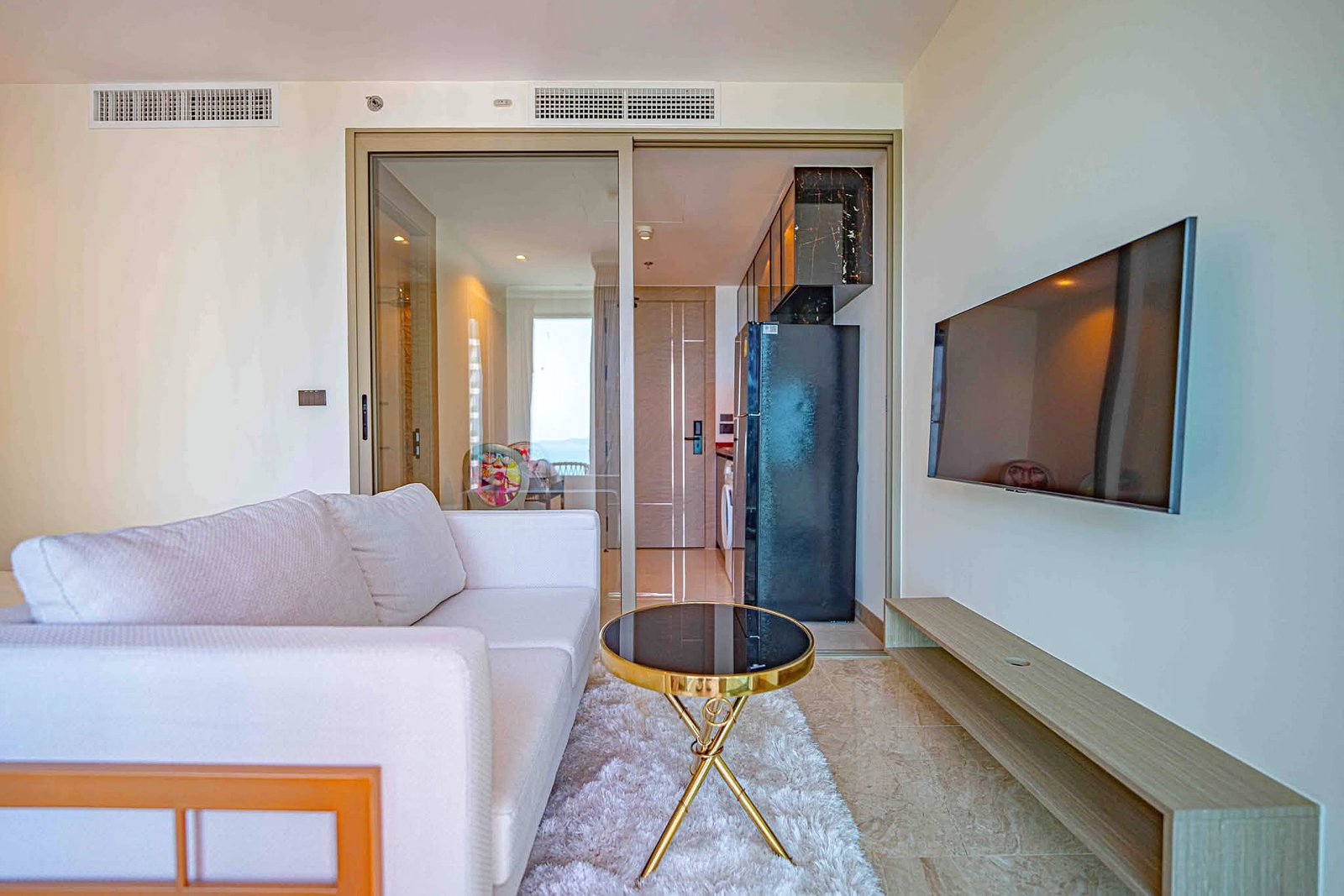 Riviera_Ocean_Drive_Studio_Rent_Rdl360_6 Modern living room with a white sectional sofa, glass sliding doors, and a wall-mounted TV on the right.