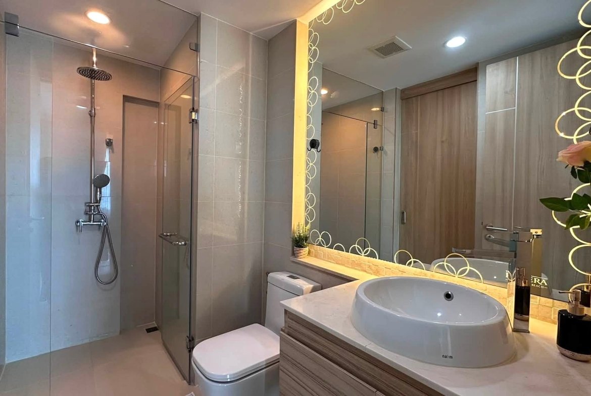 Modern bathroom with glass shower enclosure, large circular-pattern mirror, and a round vessel sink on a wood vanity.