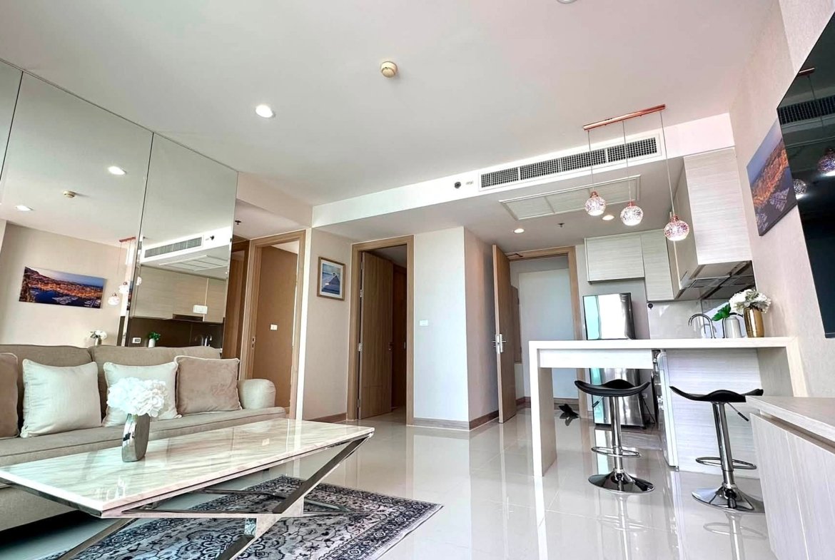 Open-plan living area with a beige sofa, marble coffee table, mirrored wall, white kitchen island, and pendant lights.