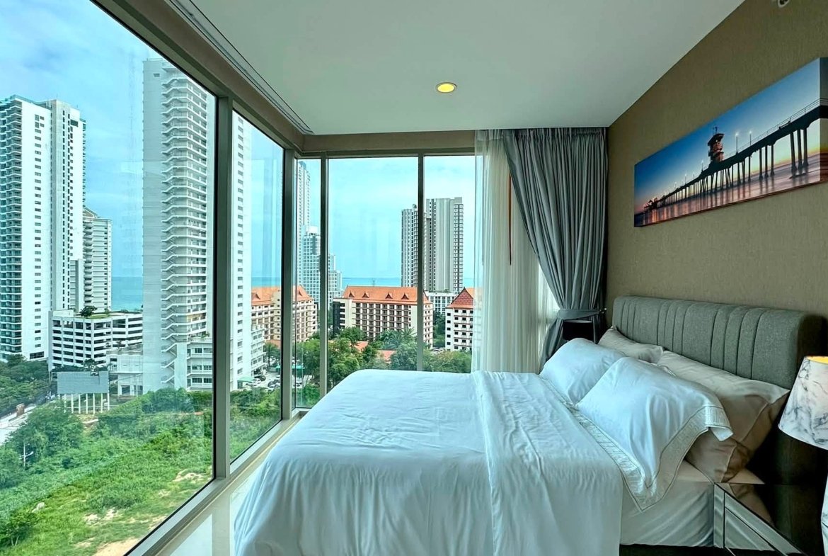 Hotel room with floor-to-ceiling windows showing city high-rises and the ocean beyond.