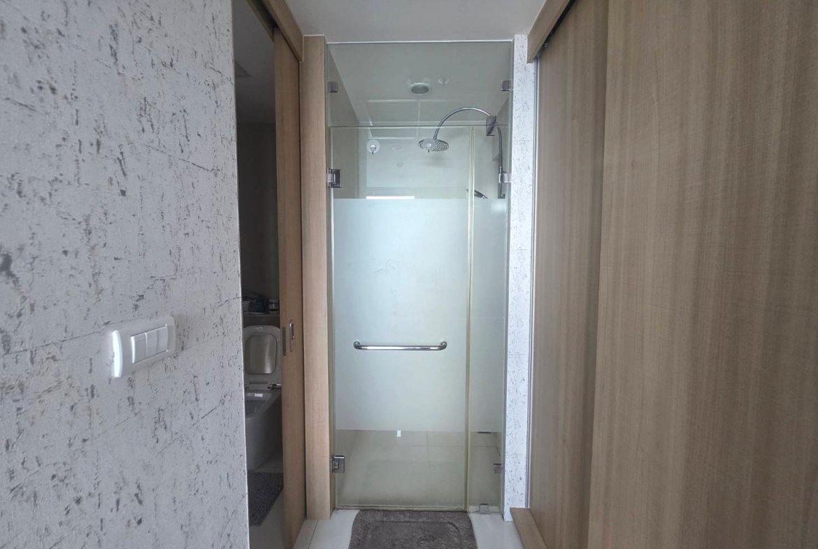 Narrow bathroom with a glass shower enclosure featuring a frosted bottom panel and chrome handle between wood-paneled walls.