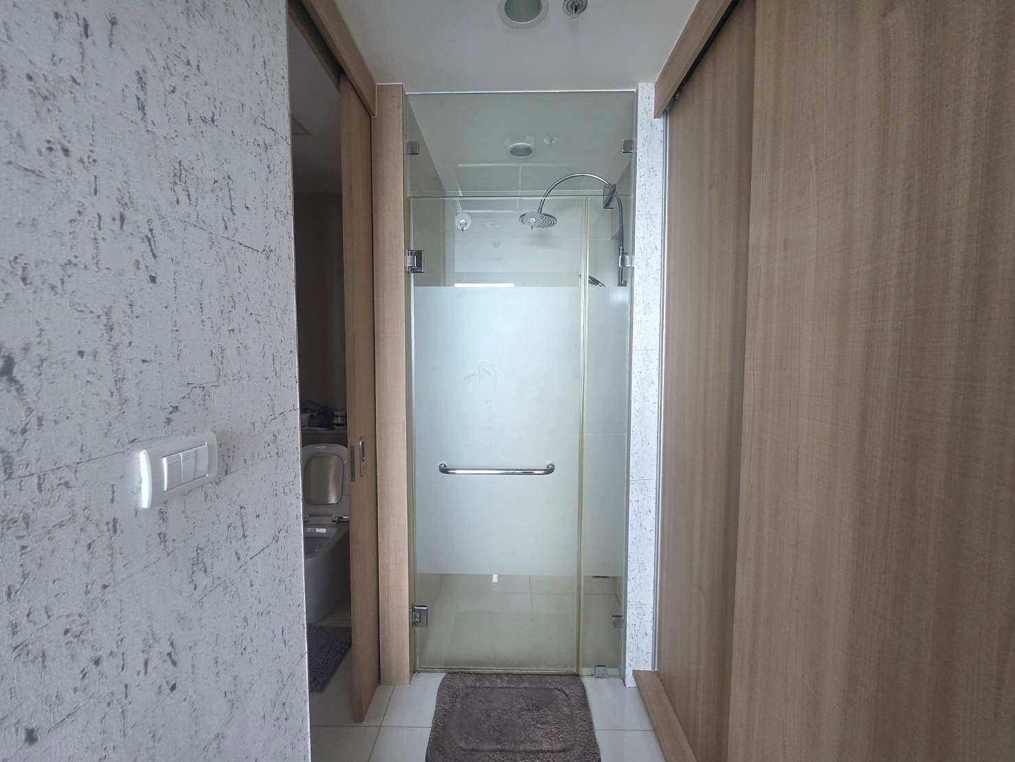 Riviera_Wongamat_B1209_5 Narrow bathroom with a glass shower enclosure featuring a frosted bottom panel and chrome handle between wood-paneled walls.