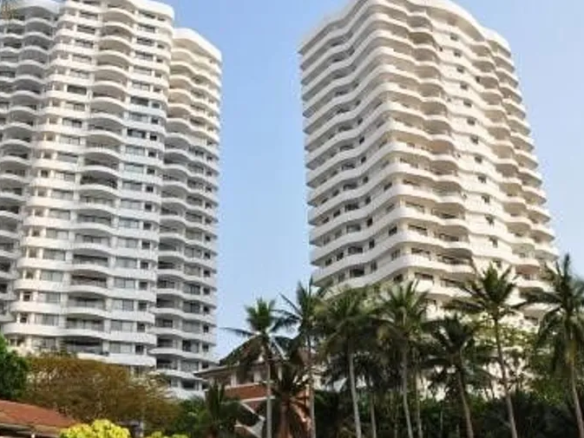 Two tall white apartment towers with curved balconies, palm trees in the foreground on a sunny day.