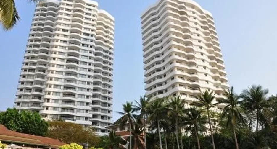 Two tall white apartment towers with curved balconies palm trees in the foreground on a sunny day