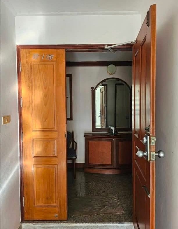Open wooden doorway revealing a small hallway with a polished wood dresser and round mirror in the back.